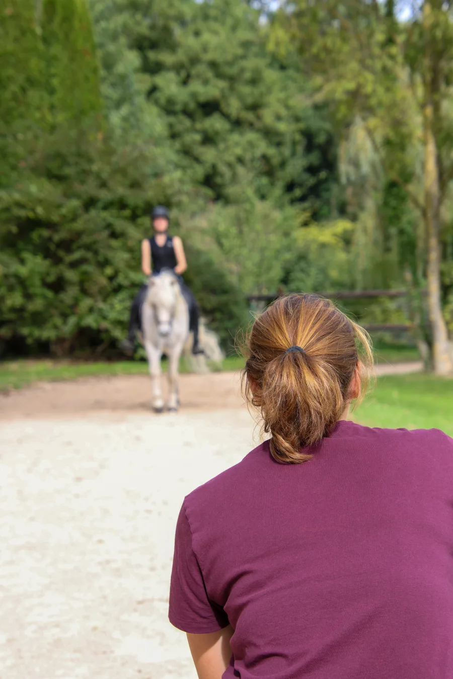 Nadine sieht einer Reiterin auf einem Schimmel beim Reiten zu
