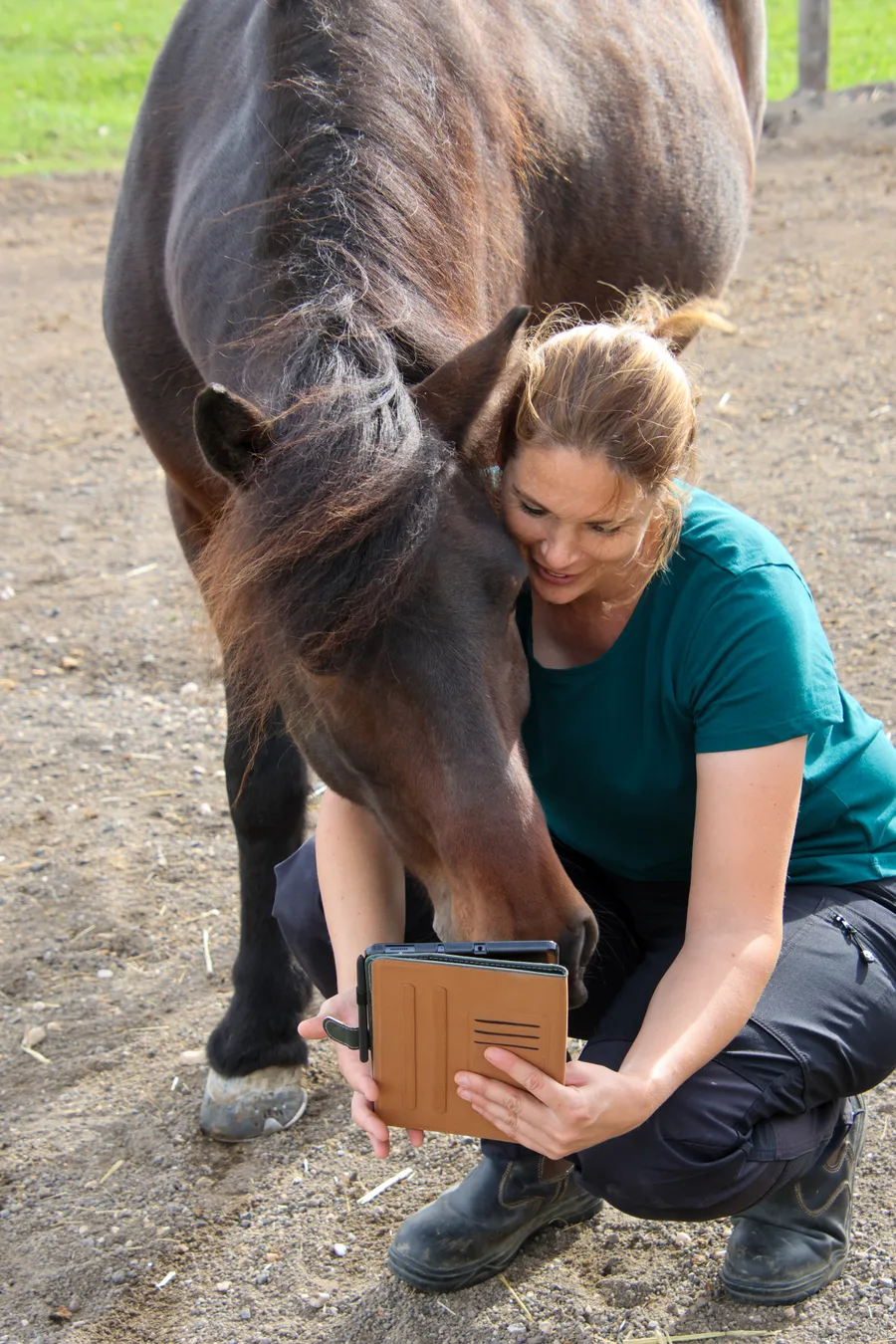 Nadine hockt neben einem Pony und zeigt ihm ein Tablet