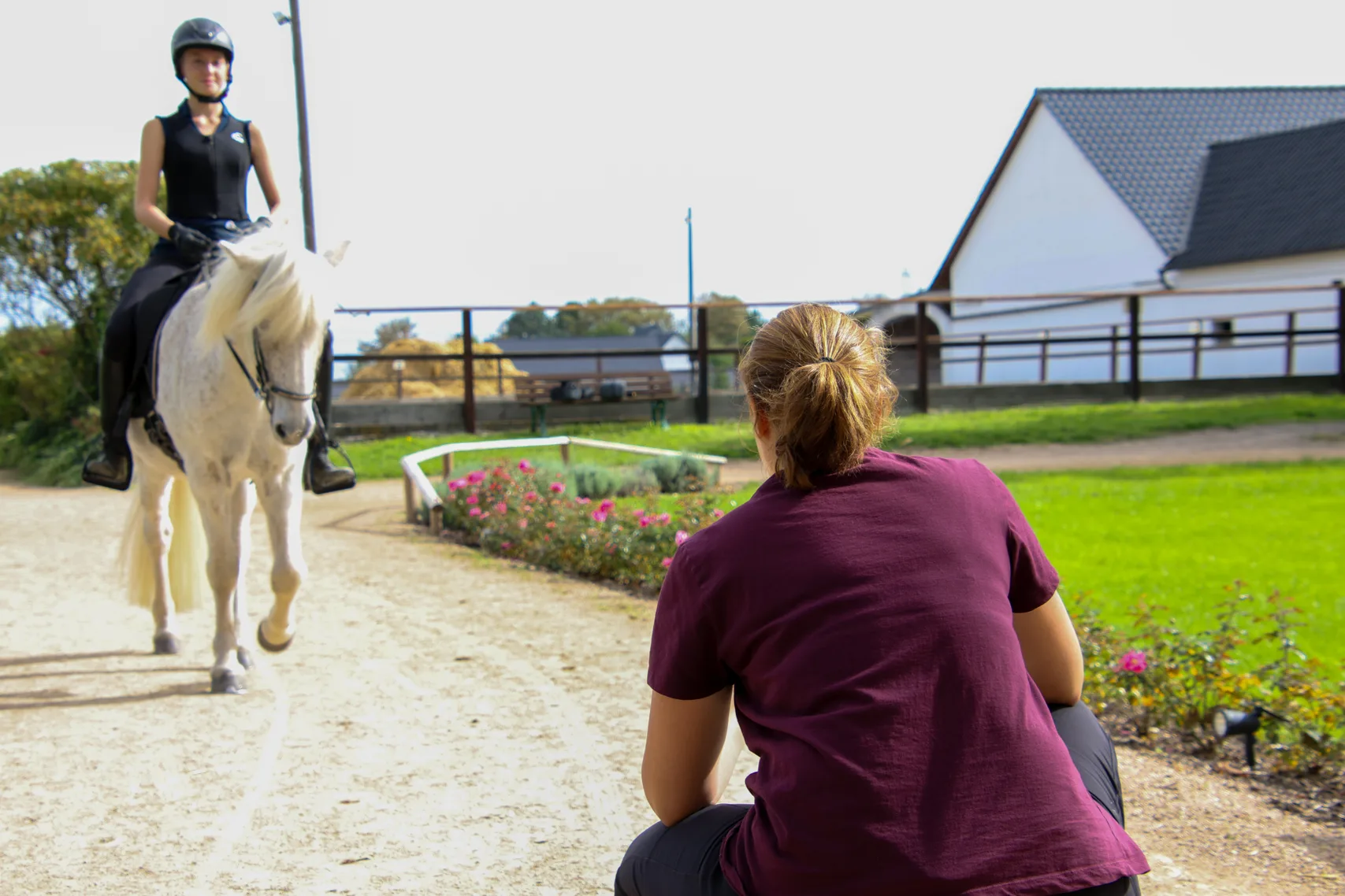 Nadine sieht einer Reiterin auf einem Schimmel beim Reiten zu